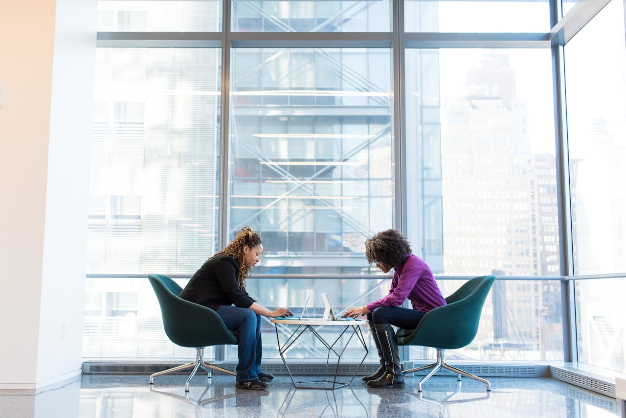 services-bg Two women engage in remote work on laptops in a bright, modern office lobby, reflecting a professional yet relaxed atmosphere.